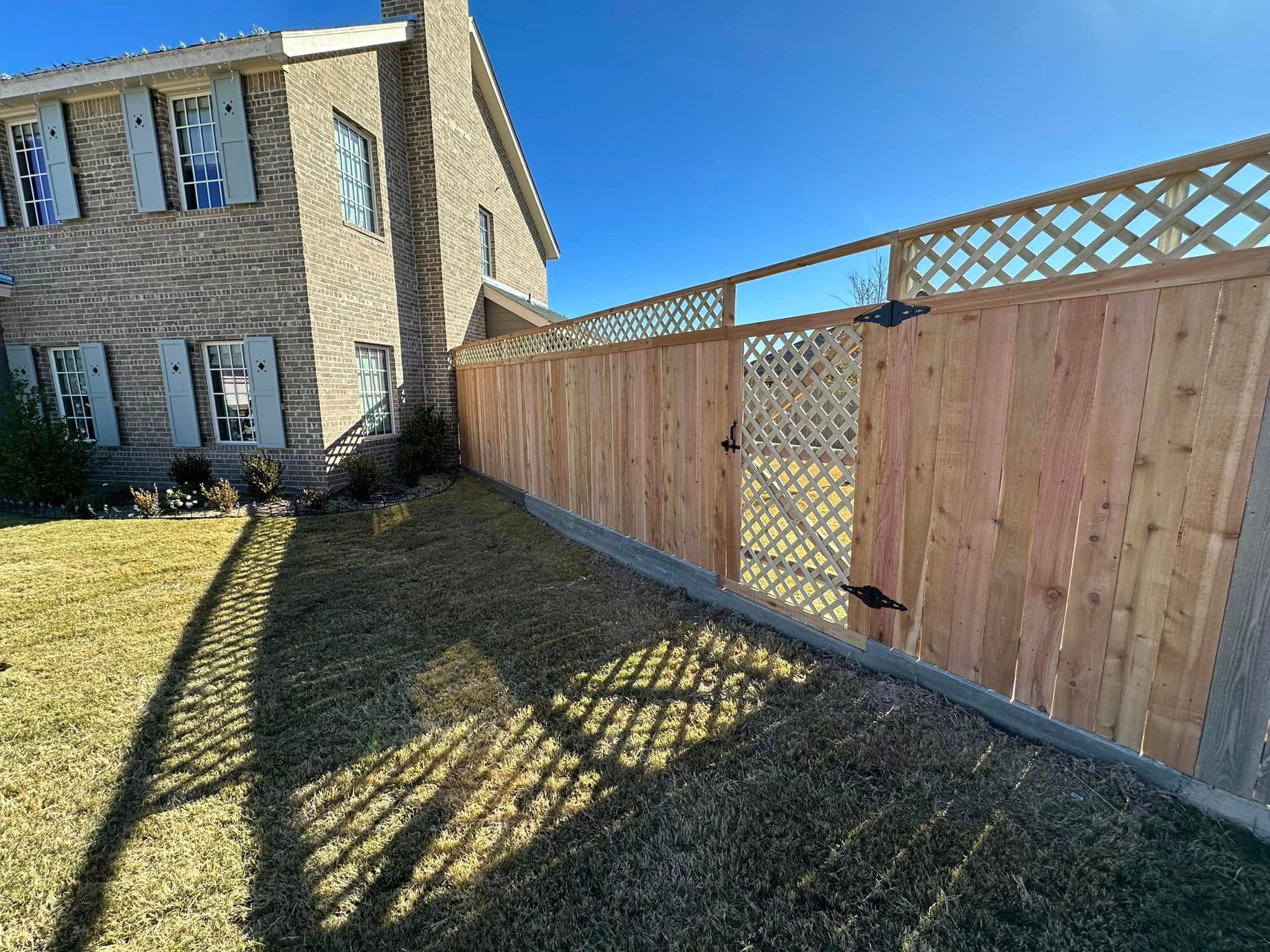 Fortress wood privacy fence and lattice gate beside a brick home