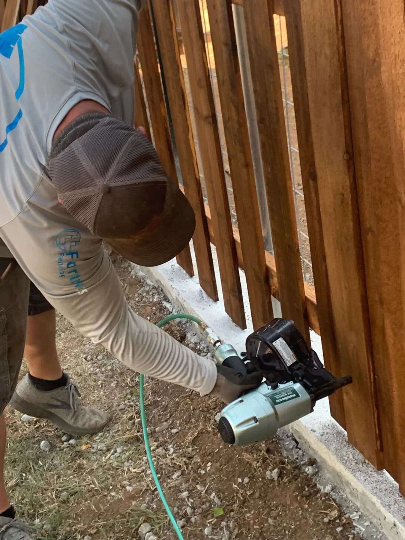 Worker fastening wood boards along a Fortress fence project